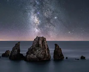 Calm Prints: Big rough cliffs on blue calm ocean during bright evening under colorful starry sky with milky way