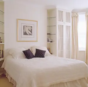 Shelving Prints: Black and white cushions on white quilt on bed in modern white bedroom with built in wardrobe and shelves