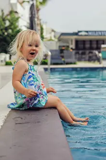 Playful Prints: blonde girl sits on swimming pool, playfully dipping feet in water
