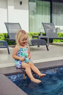 Playful Prints: blonde girl sits on swimming pool, playfully dipping feet in water