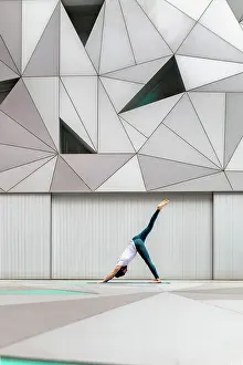 Effort Prints: Full body adult man in sportswear performing Three Legged Downward Facing Dog exercise while doing yoga against wall
