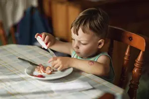 1 2 Years Old Prints: Boy sittyng by table and eating hot-dogs with fork