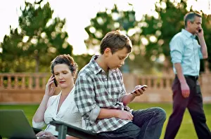 50 To 55 Years Prints: Boy text messaging on his cellphone while his parent are busy on their own cellphones