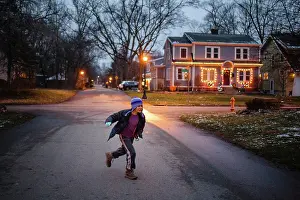 Gradeschooler Prints: A boy in winter clothes plays on lamplit street at dusk