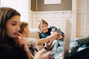 Using Phone Prints: Boys using mobile phone while sitting with female friend on sofa
