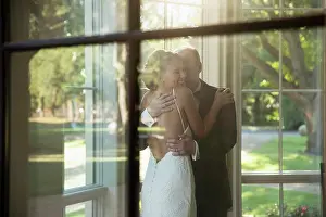 Bald Prints: Bride and father of the bride embracing celebrating the wedding day, seen through window