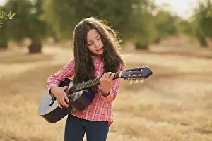 Instrument Prints: Brunette girl playing her guitar in a field of olive trees