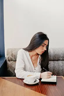 Notebook Prints: Brunette woman writing in a notebook in a bar