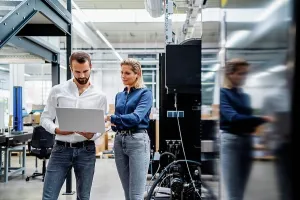 Competence Prints: Business colleagues working on laptop standing in factory