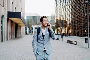 Front Of House Prints: Businessman standing with hand in pocket talking on smart phone