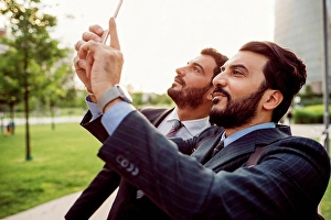 Middle Eastern Prints: Two businessmen wearing suits standing outdoors, checking their mobile phones