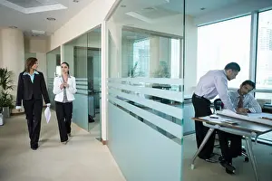 Businesswomen Prints: Businessmen working while businesswomen walking in office