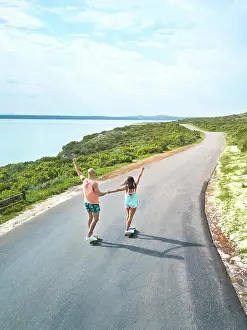 Skateboard Prints: Carefree couple riding skateboards on sunny ocean road