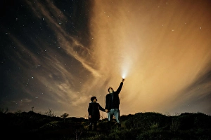 Cosmos Prints: Carefree dad and son holding hands and observing starry sky while looking up and lighting with torch at night