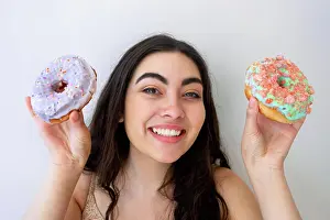 Playful Prints: Carefree woman having fun and playing with glazed pastry with sprinkles while standing by white wall