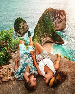 Wanderlust Prints: Carefree young couple on vacation in light casual wear lying down on peak of rough cliff