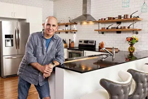 Beginnings Prints: Caucasian man standing at the edge of kitchen looking into camera smiling
