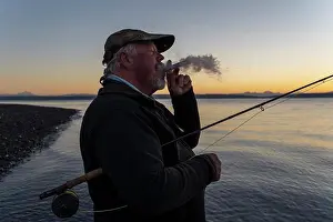 Smoking Prints: A Caucasian senior fly fisherman enjoys a sunrise cigar before fly fishing for searun coastal cutthroat trout