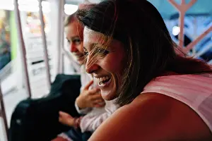 Cheerful Prints: Cheerful adult woman smiling and looking away while riding Ferris wheel with daughter in amusement park