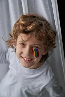 Paint Prints: From above cheerful boy with rainbow under eye smiling looking at camera at home during quarantine