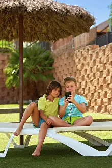 Deckchair Prints: Cheerful boys browsing smartphone on sunbed