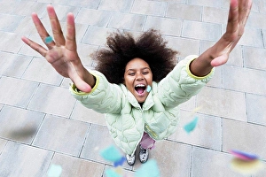 Light Hearted Prints: Cheerful girl with arms raised standing amidst confetti falling on footpath