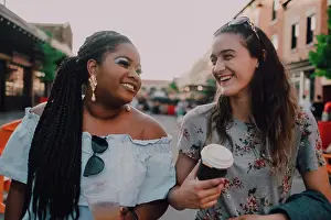 Beverage Prints: Cheerful trendy multiracial young casual women talking and drinking coffee while walking on street on sunset