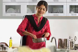 Positive Emotion Prints: Cheerful woman washing a frying pan in kitchen at home