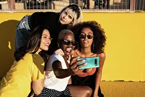 Diverse Prints: Cheerful young diverse female friends taking selfie on smartphone in street