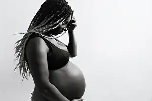 Maternity Prints: Cheerful young pregnant black female with braids touching belly