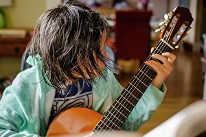 Concentrate Prints: A child with hair hanging in his face practices classical guitar