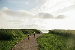 Soft Light Prints: Children running on a path towards the sea with a boat in the distance