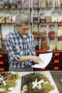 Trade Prints: China, Hong Kong, Sheung Wan, Chinese Medicine Shop, Pharmacist Checking Prescription List