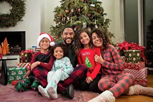 Small Group Of People Prints: Christmas Card Portrait of a joyful young Black family sitting in front of Christmas tree