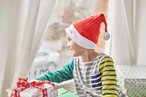 Curiosity Prints: Christmas morning in a family home. A boy in a Santa hat looking out of a bedroom window
