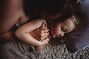 Gradeschooler Prints: Close up of hands together of mother kissing her daughter in bed