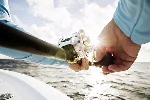 Florida Prints: Close up shot of mans hands reeling in fishing rod with sunburst