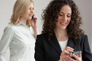 Businesswomen Prints: Close-up of a businesswoman using a PDA with another businesswoman talking on a mobile phone