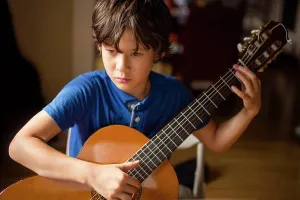 Focused Prints: Close-up of a focused boy practicing classical guitar in window light