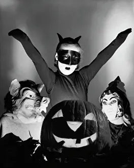 Shoulders Prints: Close-up of an illuminated jack o lantern with three people wearing Halloween costumes behind it