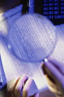 Newspaper Prints: Close-up of a person's hand holding a magnifying glass over a newspaper