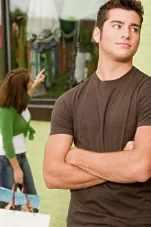 Consumerism Prints: Close-up of a teenage boy looking sideways with a young woman shopping behind him