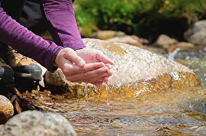 Hike Prints: Close-up of water drops falling from female hands into a stream
