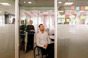 Disability Prints: Colleagues looking at businessman sticking adhesive notes on glass wall in board room
