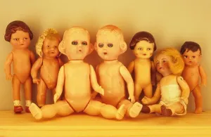 Human Representation Prints: Collection of seven small early to mid-20th century traditional baby dolls lined up on wooden shelf