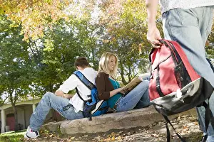 Two college friends sitting back to back at park