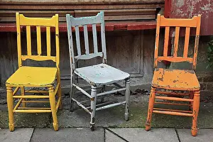 Exterior Photograph Prints: Three colourful old wooden chairs on a pavement in front of a house