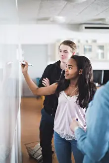 Stockholm Prints: Confident girl writing on whiteboard while standing amidst teacher and friend in classroom