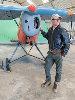 Pilot Prints: Confident pilot beside retro plane in hangar