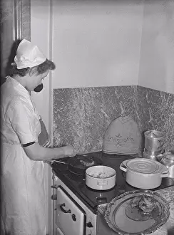 Cooking in the 1940s. A young woman employed as a house maid is cooking a meal on the kitchen stove